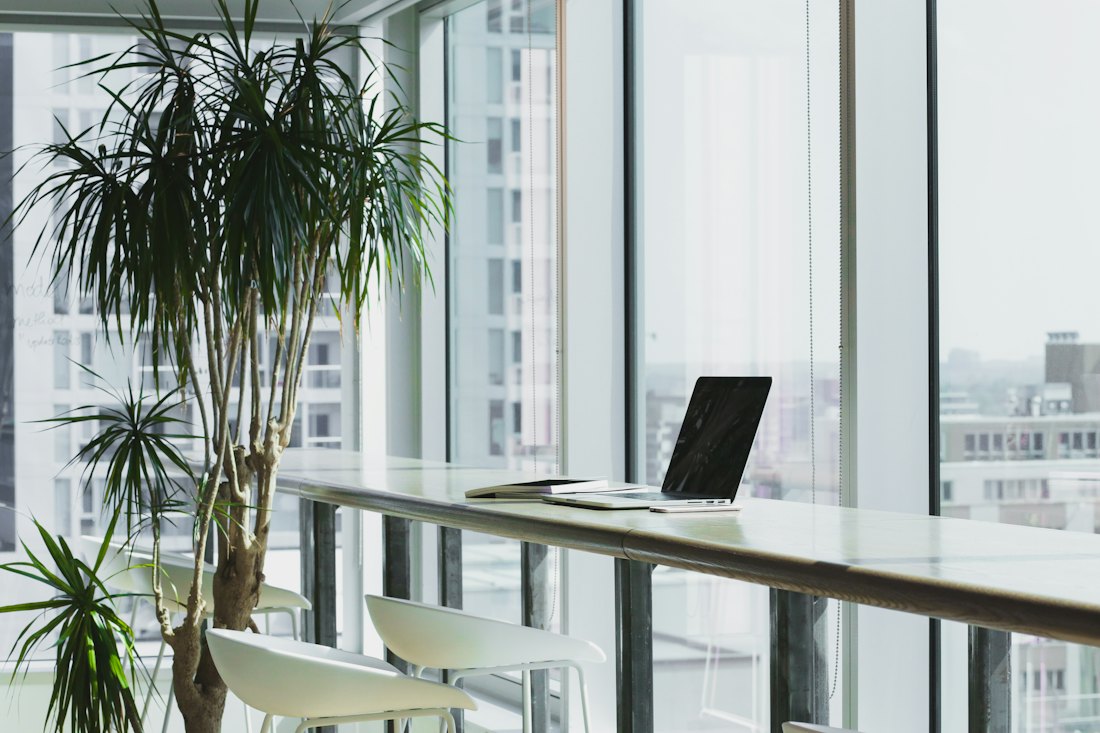 An empty desk by a window in a quiet office, laptop open